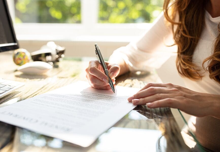 Close-up of a woman signing an entertainment contract at a desk, symbolizing key legal clauses explained in film and media agreements.